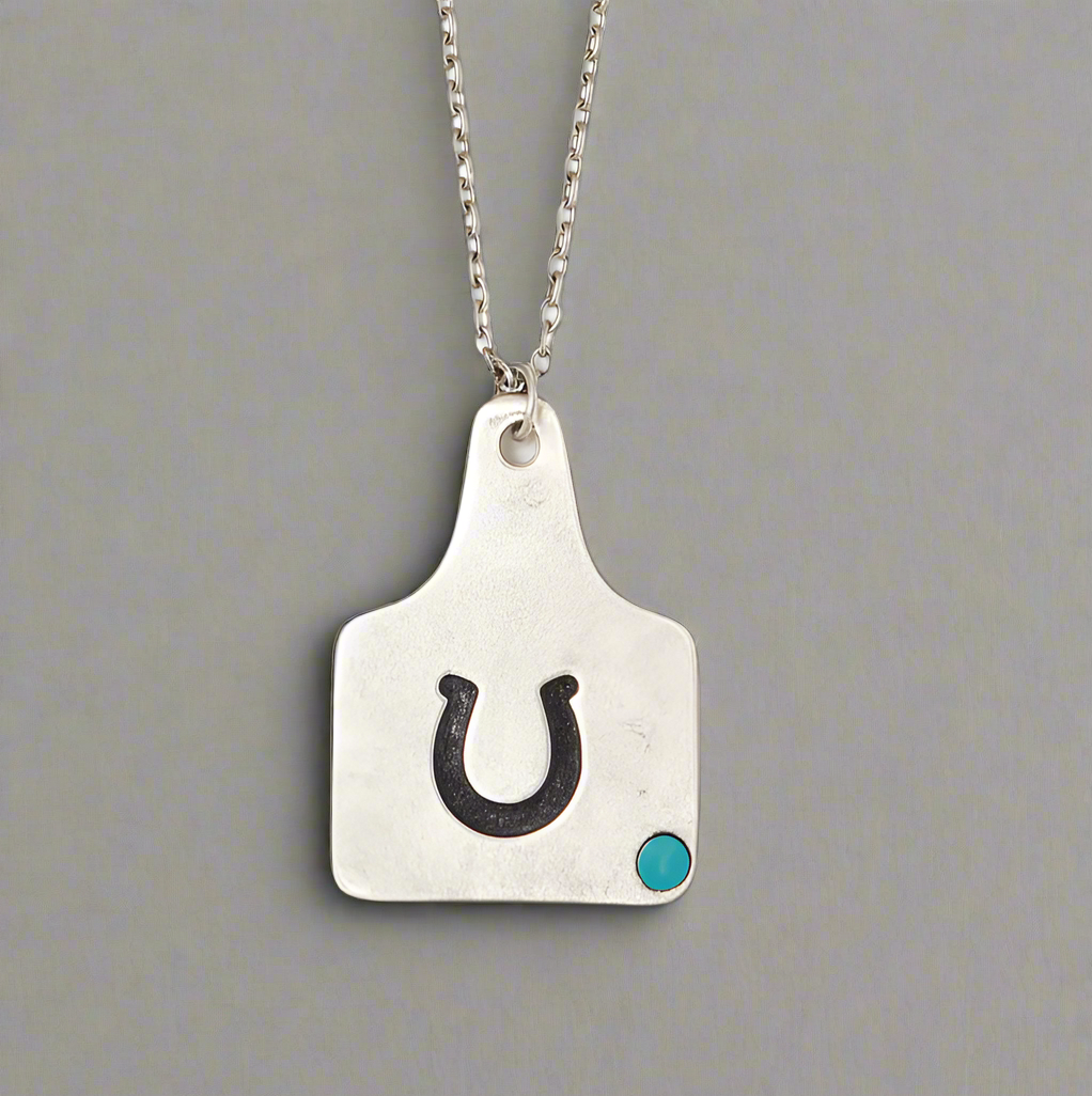 Silver pendant with a horseshoe and turquoise stone.